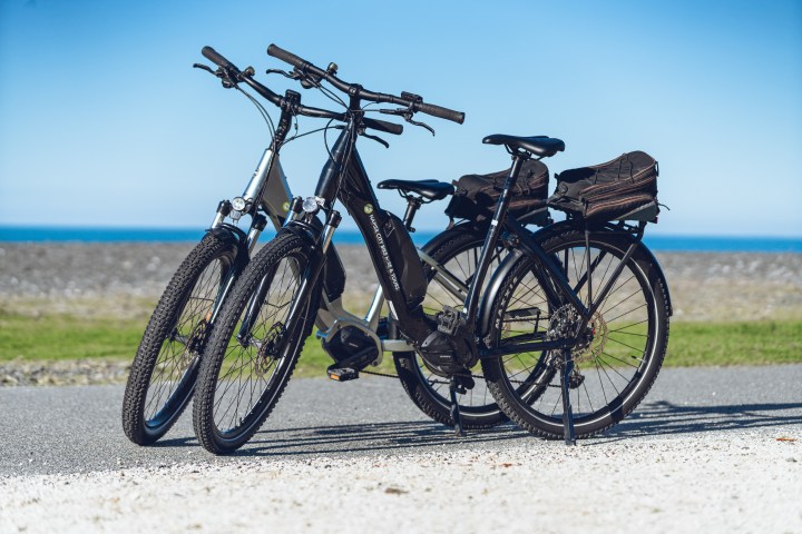 Two electric bikes parked on a sunny path by the sea.