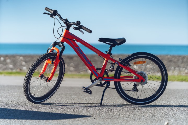 Red bicycle parked on pavement near the beach.