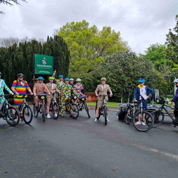 Group of cyclists in colorful costumes posing with bikes on a cloudy day.