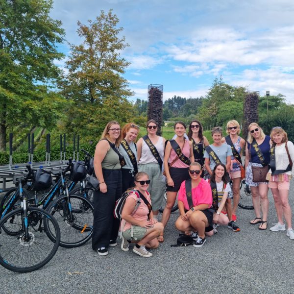 Group of women with sashes posing near bicycles in a park on a Napier City Bike Hire group tour