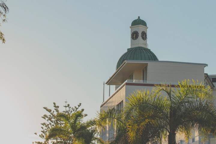 Building with clock tower, palm trees, and clear sky at sunset.