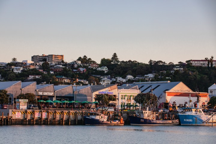 Harbor with boats docked, buildings, and hillside houses at sunset.