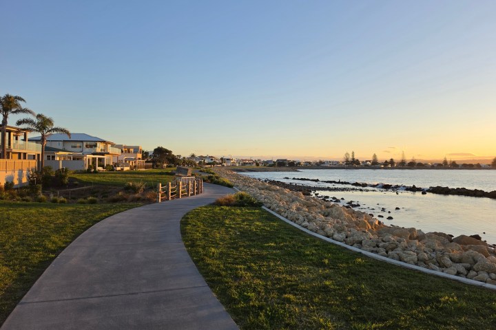 Coastal walkway beside water, with houses and trees at sunset.